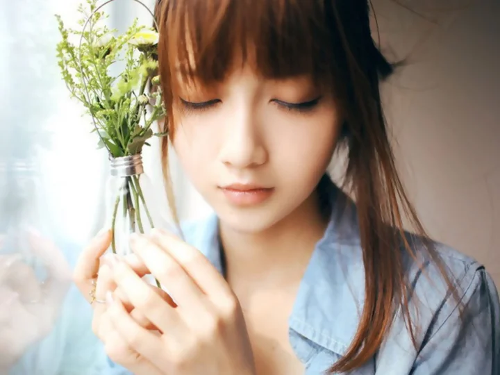 目を閉じた女性が室内で葉のついた小さな花束を持っている。