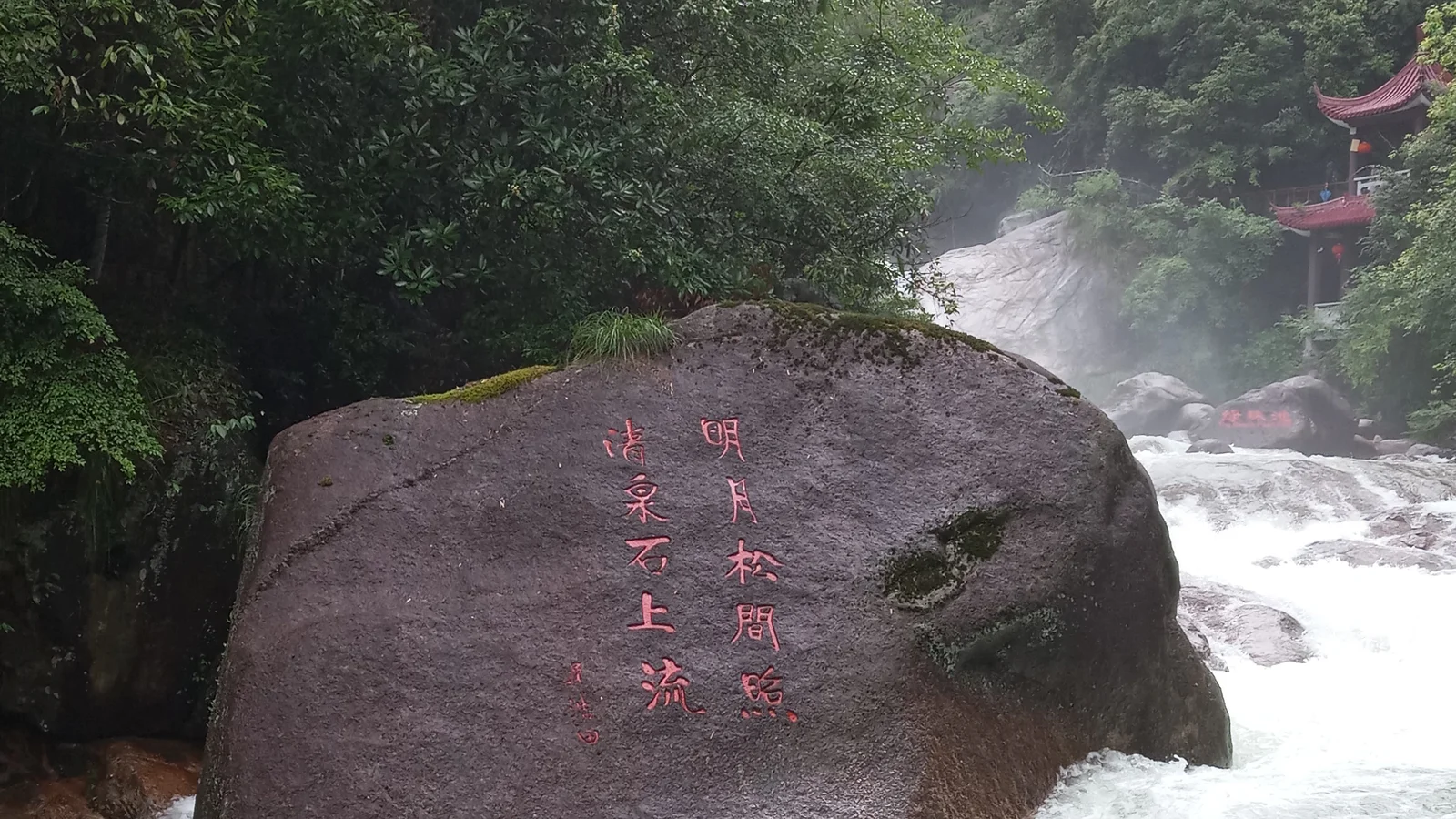 森林中的瀑布從刻有紅色漢字的巨石旁奔流而下。