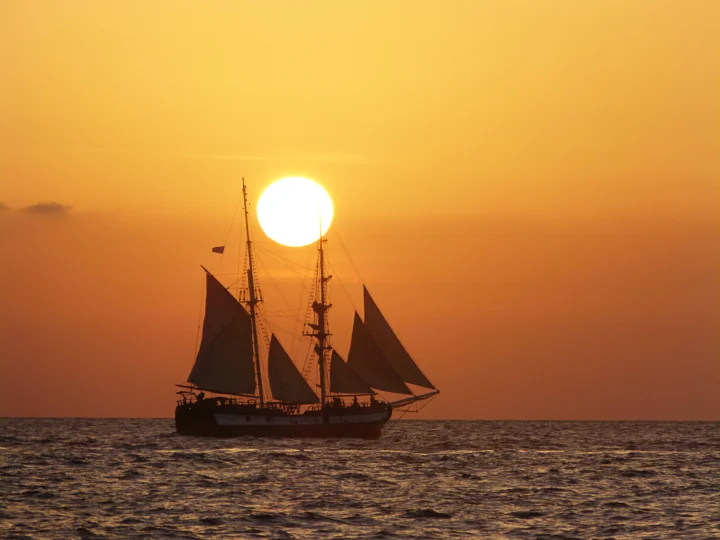 一艘帆船航行在夕阳映照的海面上。