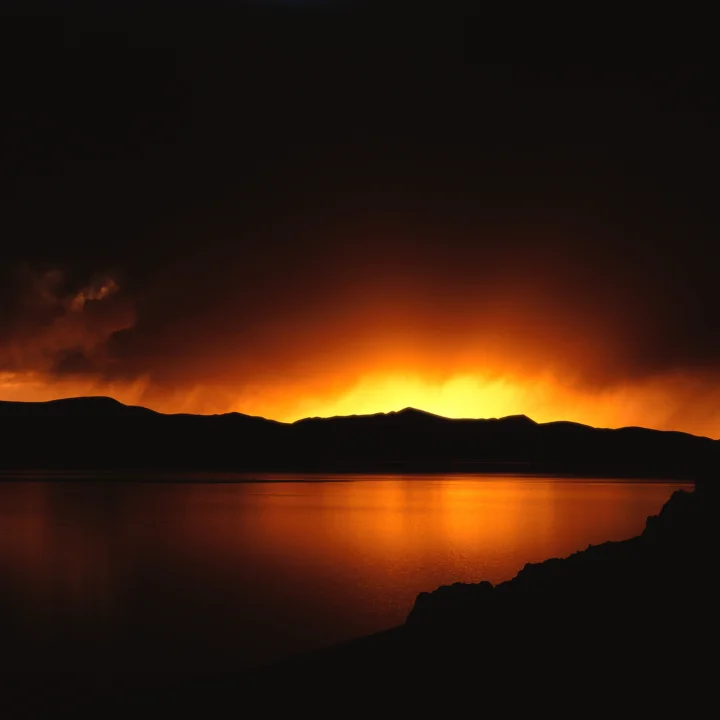 橙色夕阳映照着湖面，远处是连绵的山脉剪影。