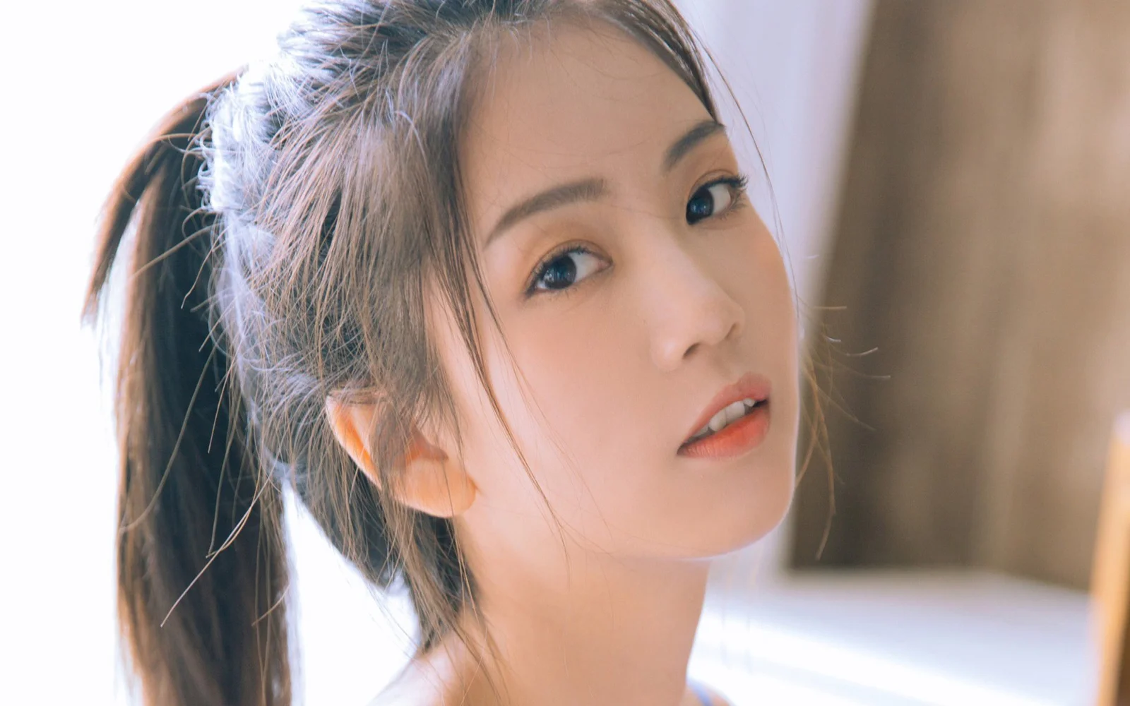 一名綁著馬尾的成年女性在柔和光線下近距離望向鏡頭。