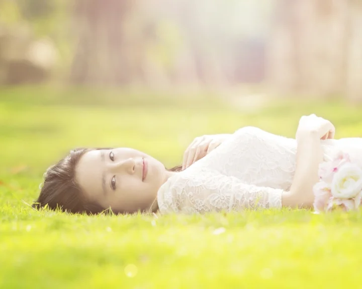 一名身穿白色蕾丝服装的女子躺在明亮的绿色草地上。
