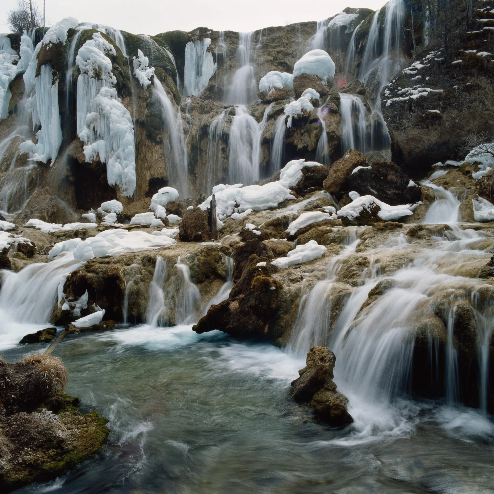 冰雪覆盖的层叠瀑布从岩石间流入清澈溪水。