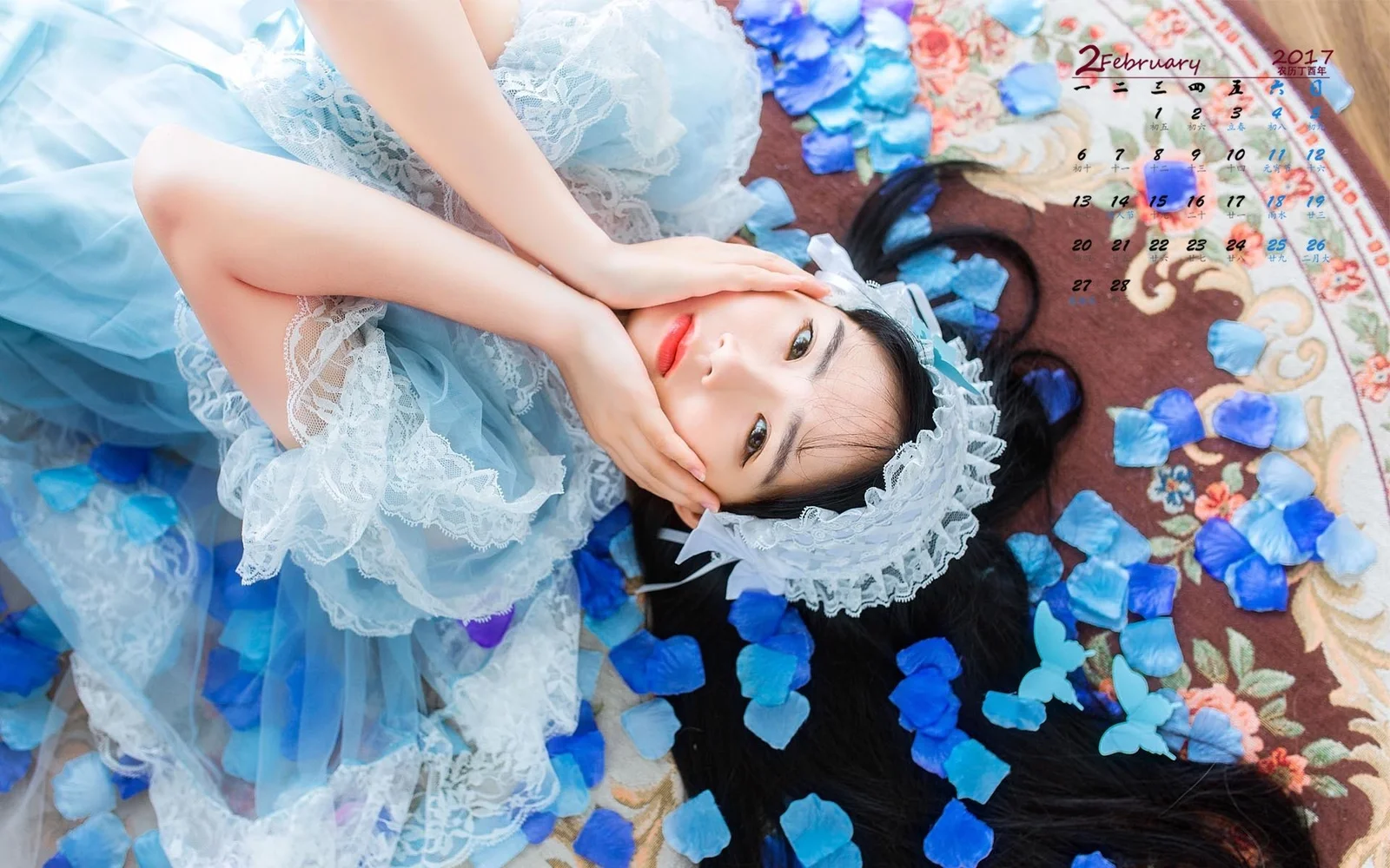 青いワンピースを着た成人女性が花柄のラグの上に横たわっています。