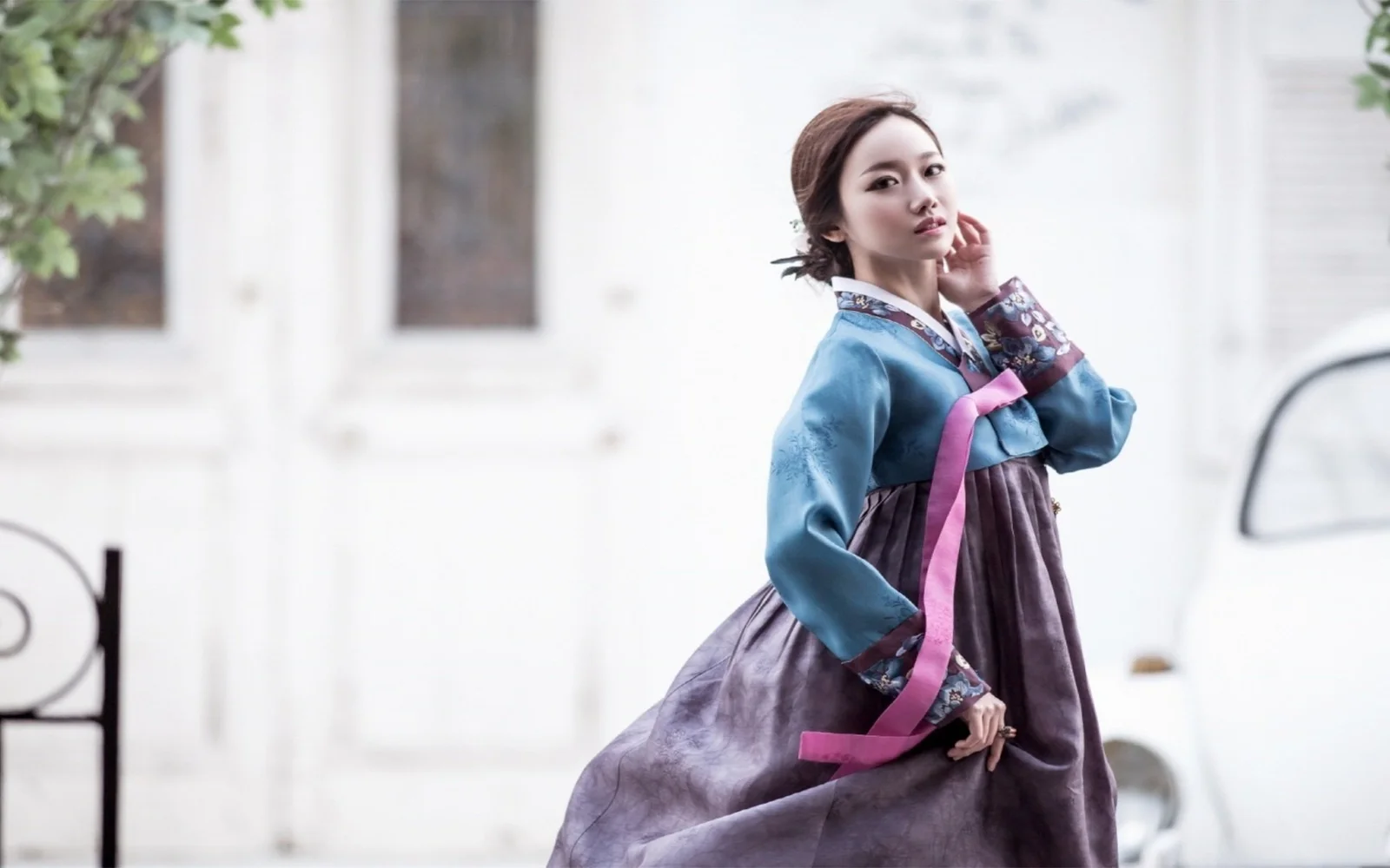 一名成年女子身穿蓝紫色韩服站在明亮的浅色建筑前。