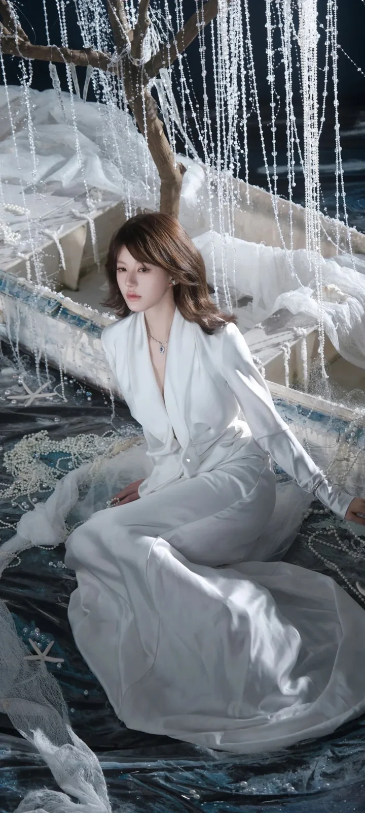 一名成年女性穿着白色长裙坐在垂落的珠帘装饰之间。