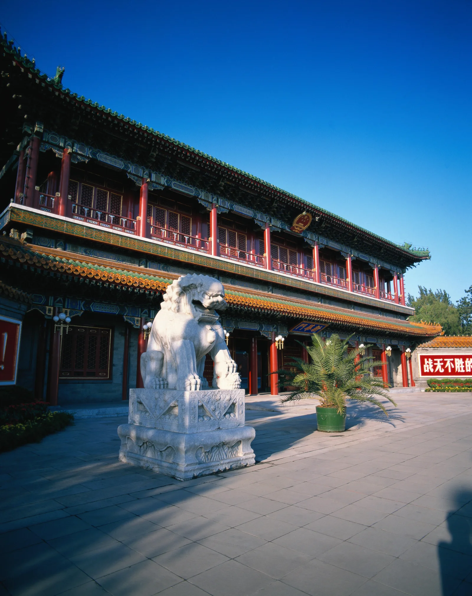 蓝天下，一座彩绘中式古建筑与石狮子坐落在开阔庭院中。