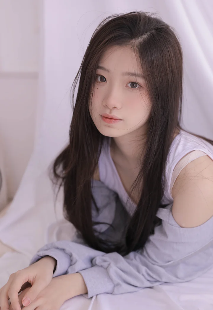 一名长发女性身穿浅紫色服装坐在室内柔和的紫色背景前。