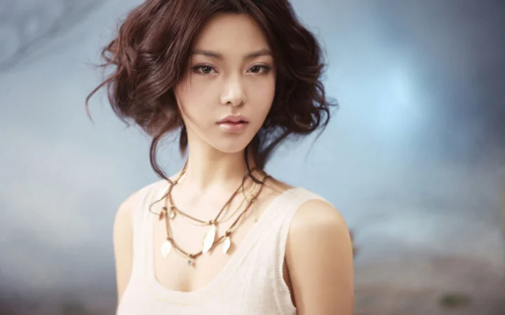 짧은 곱슬머리와 여러 겹의 목걸이를 한 여성을 정면으로 담은 인물 사진입니다.