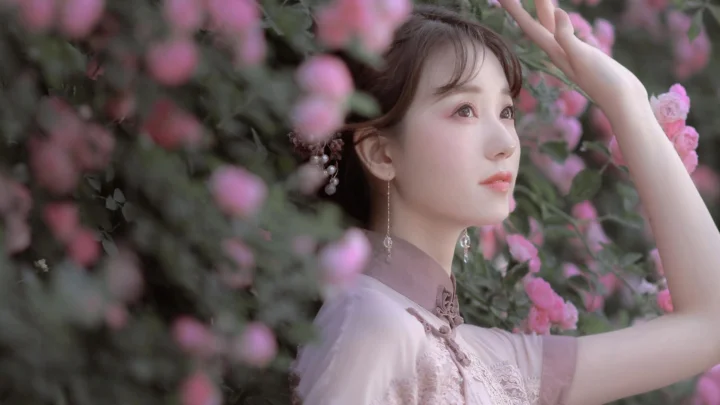 一名女子站在盛开的粉色花朵间抬手眺望。