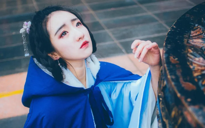 一名身穿蓝色传统服饰的女子坐在石阶旁，面向镜头。