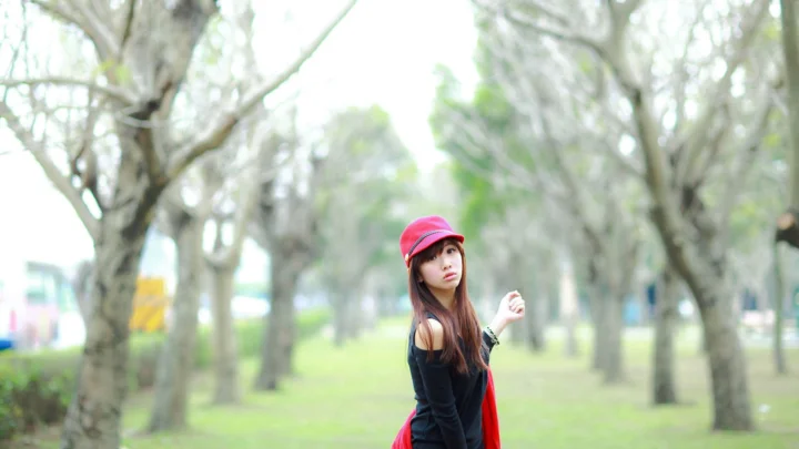 一名戴红色帽子的女子站在树木环绕的公园中。
