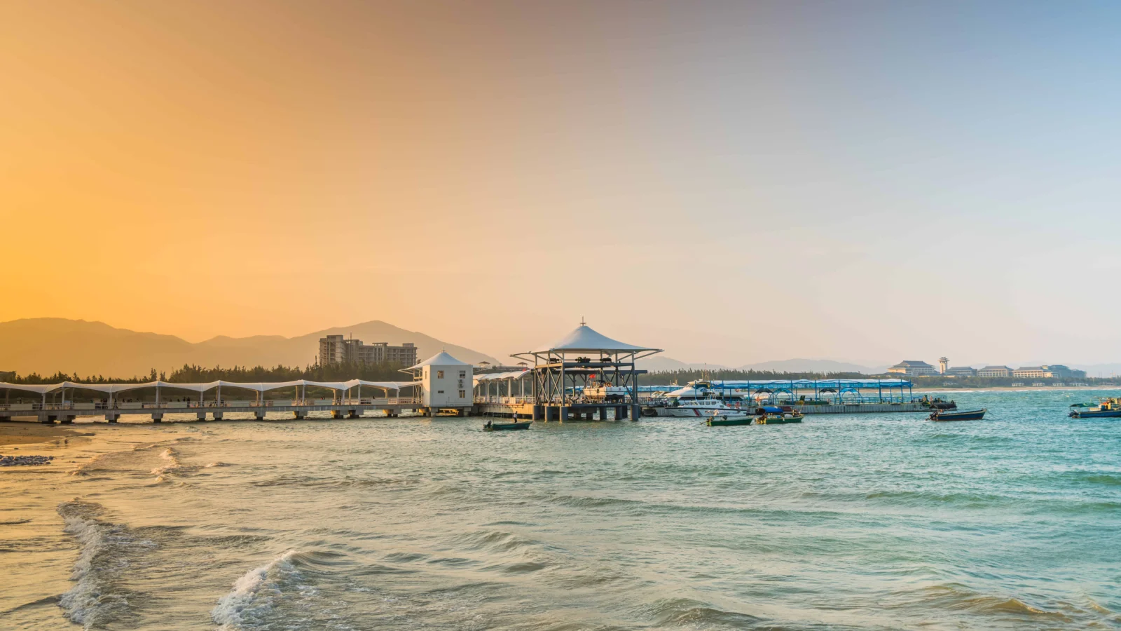 夕阳映照下的海滨码头、海水与远山构成宁静的海岸风景。