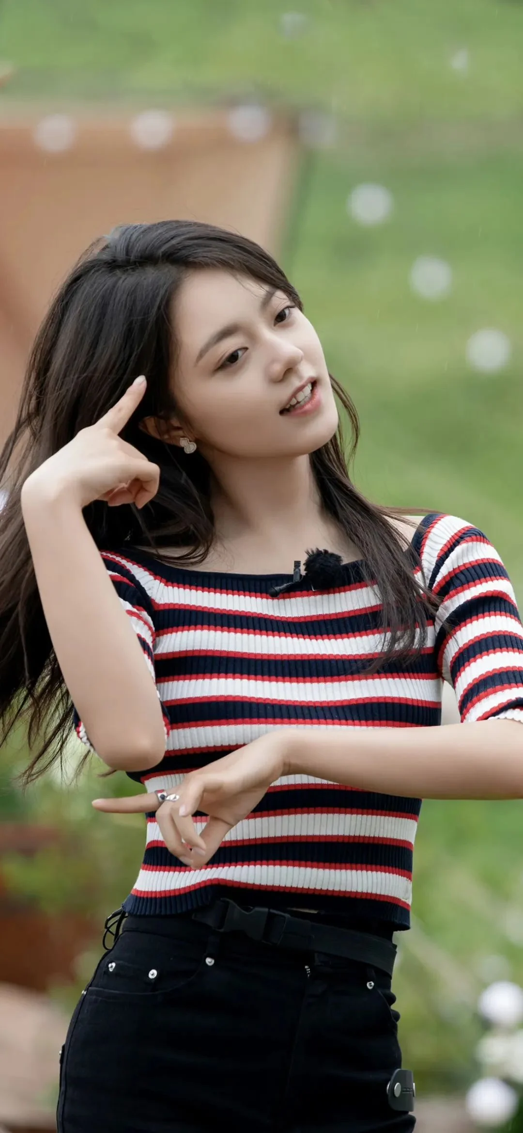 一名女子站在户外绿意背景前，穿着条纹上衣并面向镜头微笑。