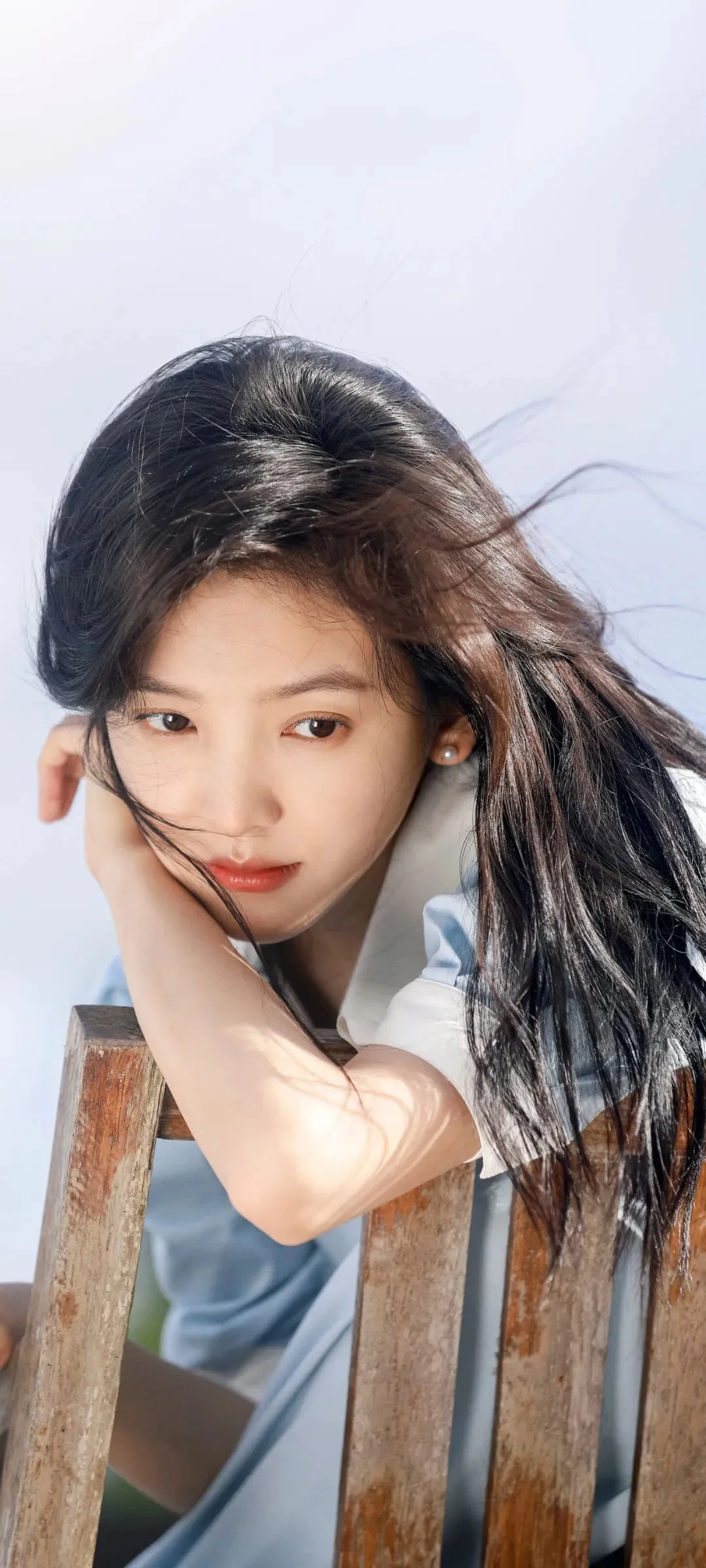 긴 머리의 여성이 나무 의자에 기대어 햇빛을 받고 있습니다.