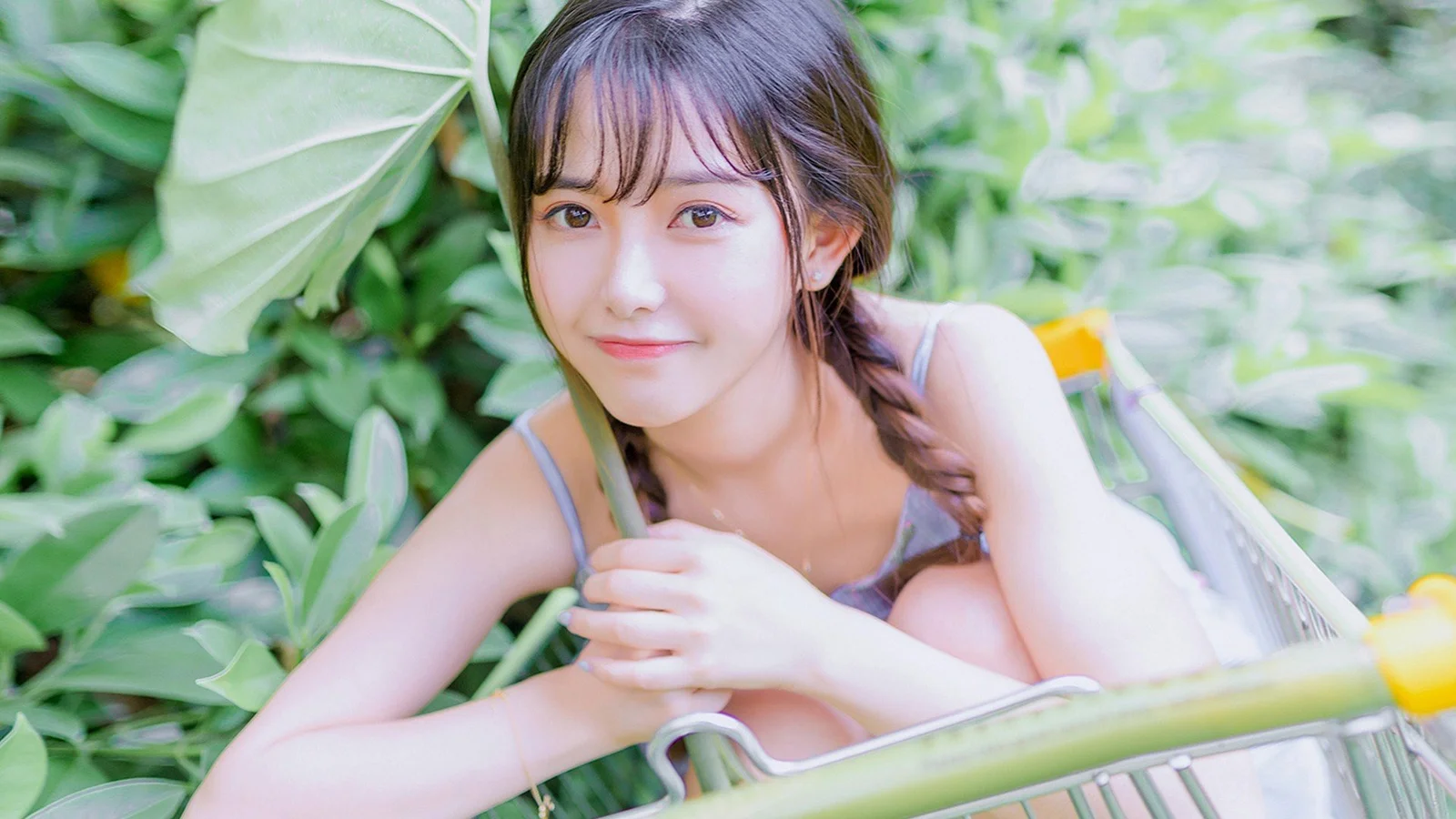 女性が茂った緑の葉と自転車のそばでカメラを見ています。