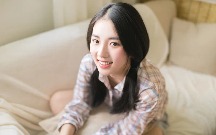一名成年女子坐在沙发上微笑看向镜头。