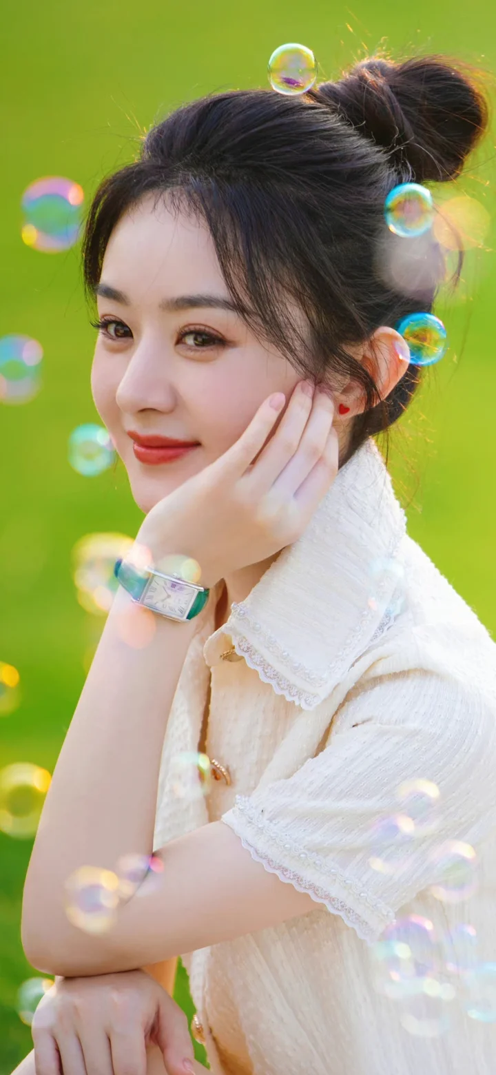 一位身穿白色上衣的女性在绿色背景前托腮微笑，周围漂浮着彩色泡泡。