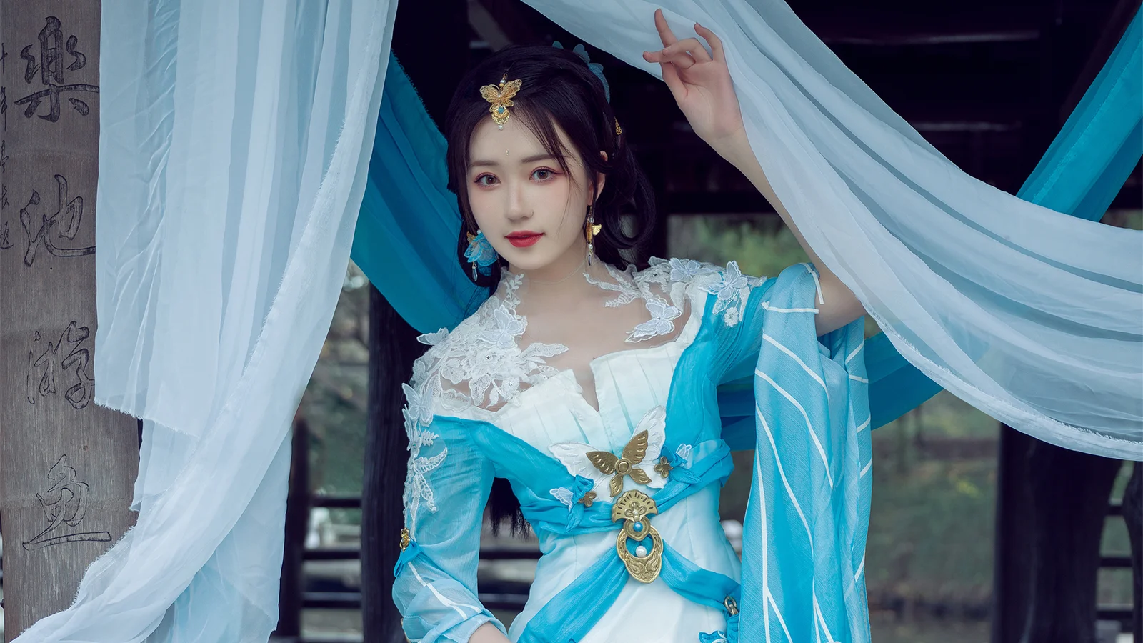 一位身穿蓝白色传统服饰的女子站在飘动的白色与蓝色布幔之间。