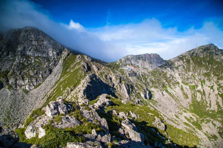 陡峭的岩石山峰和绿色山坡在蓝天白云下延展开来。