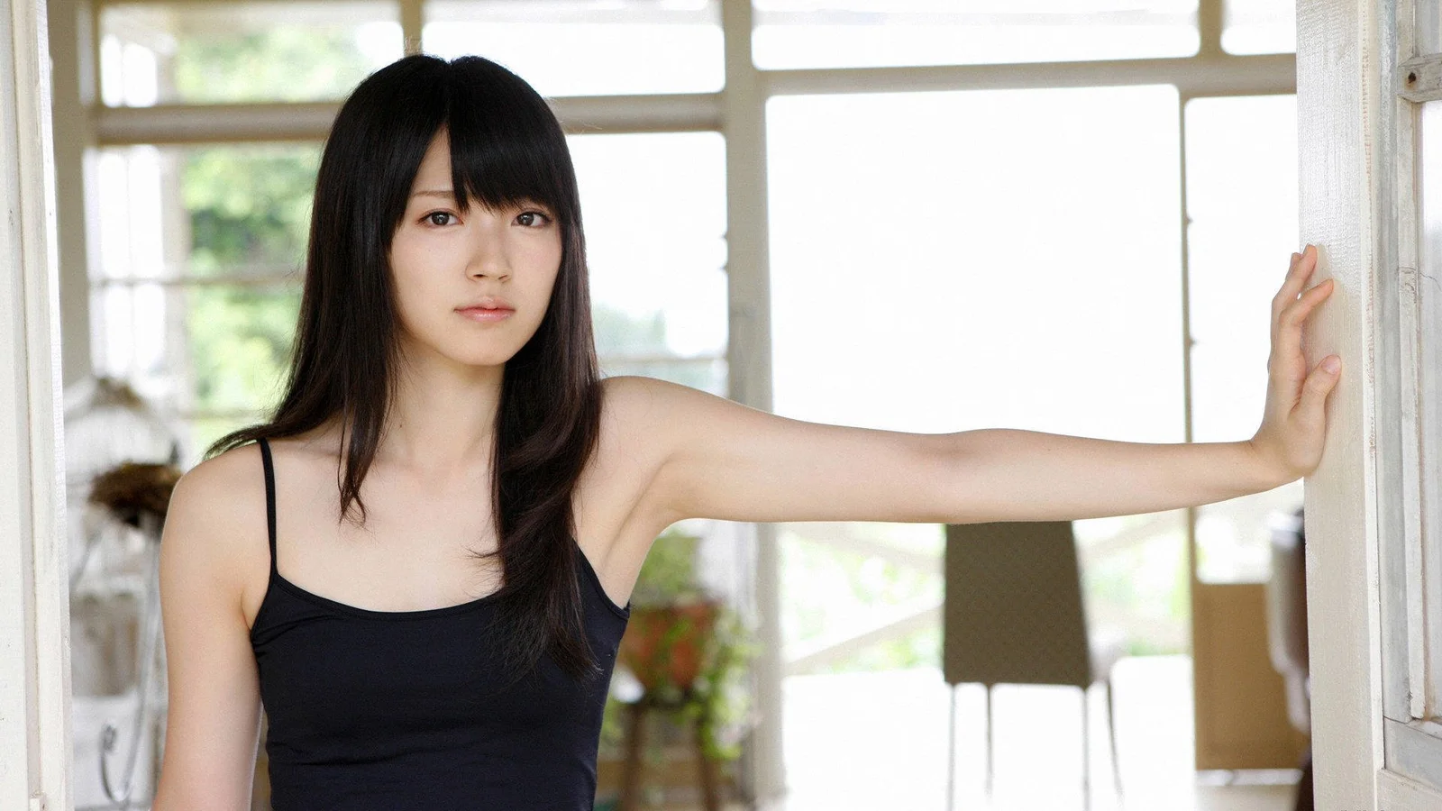 一名长发女性站在明亮窗边，伸手扶着门框。