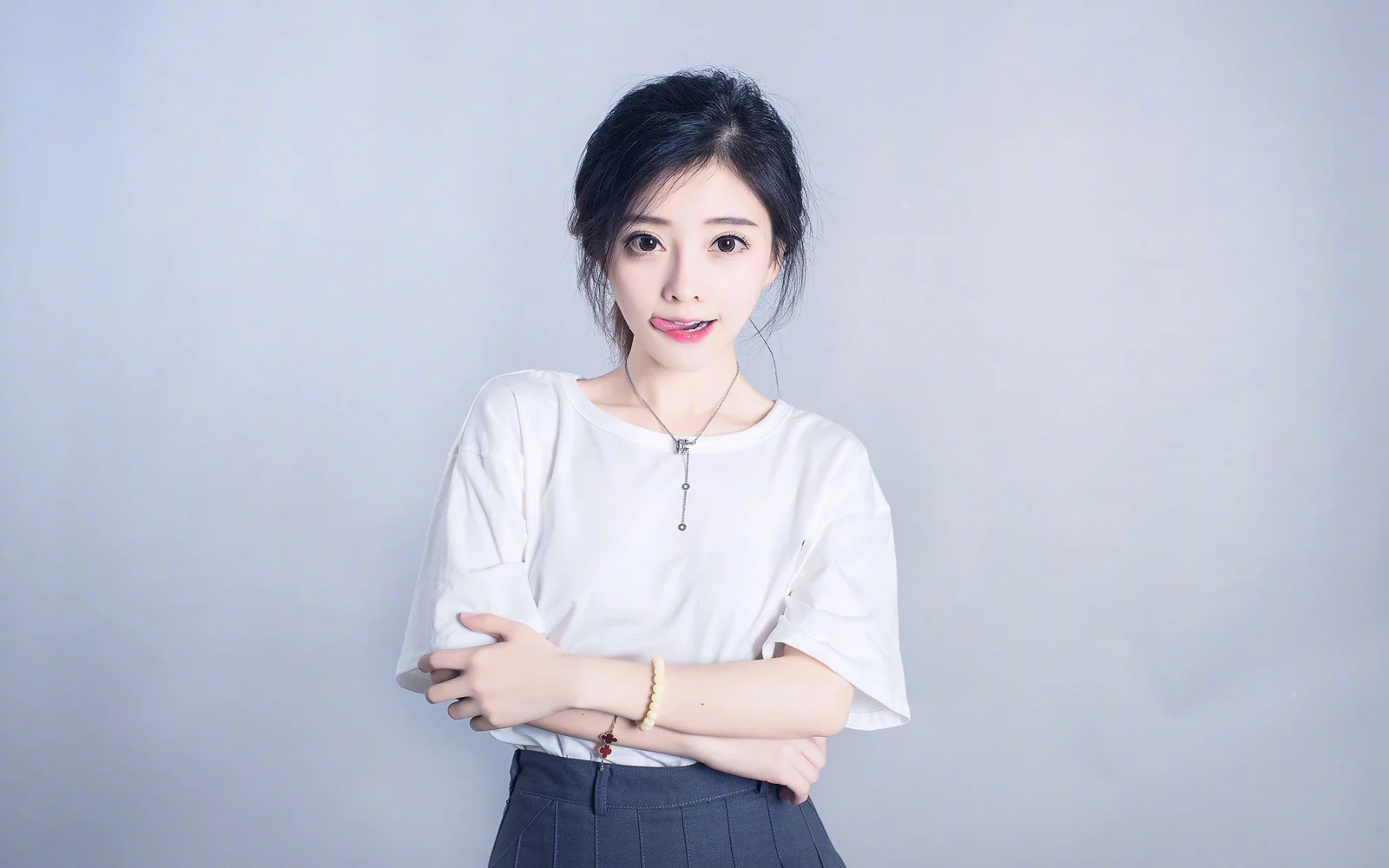 一名成年女性穿着白色上衣站在浅灰色背景前，双臂交叠面对镜头。