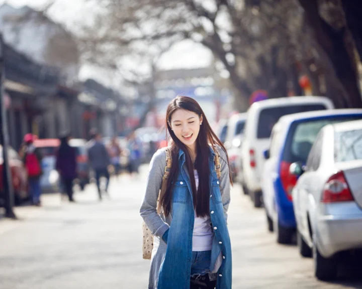 一名年轻女性背着背包微笑走在阳光明媚的城市街道上。
