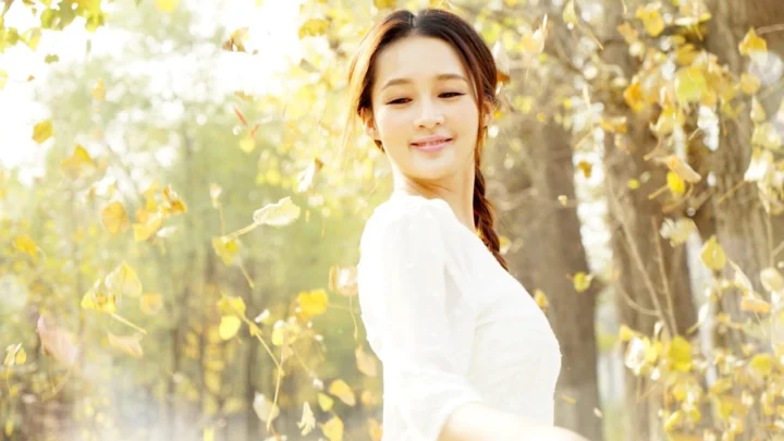 一名成年女性站在金色树叶环绕的秋日森林中。