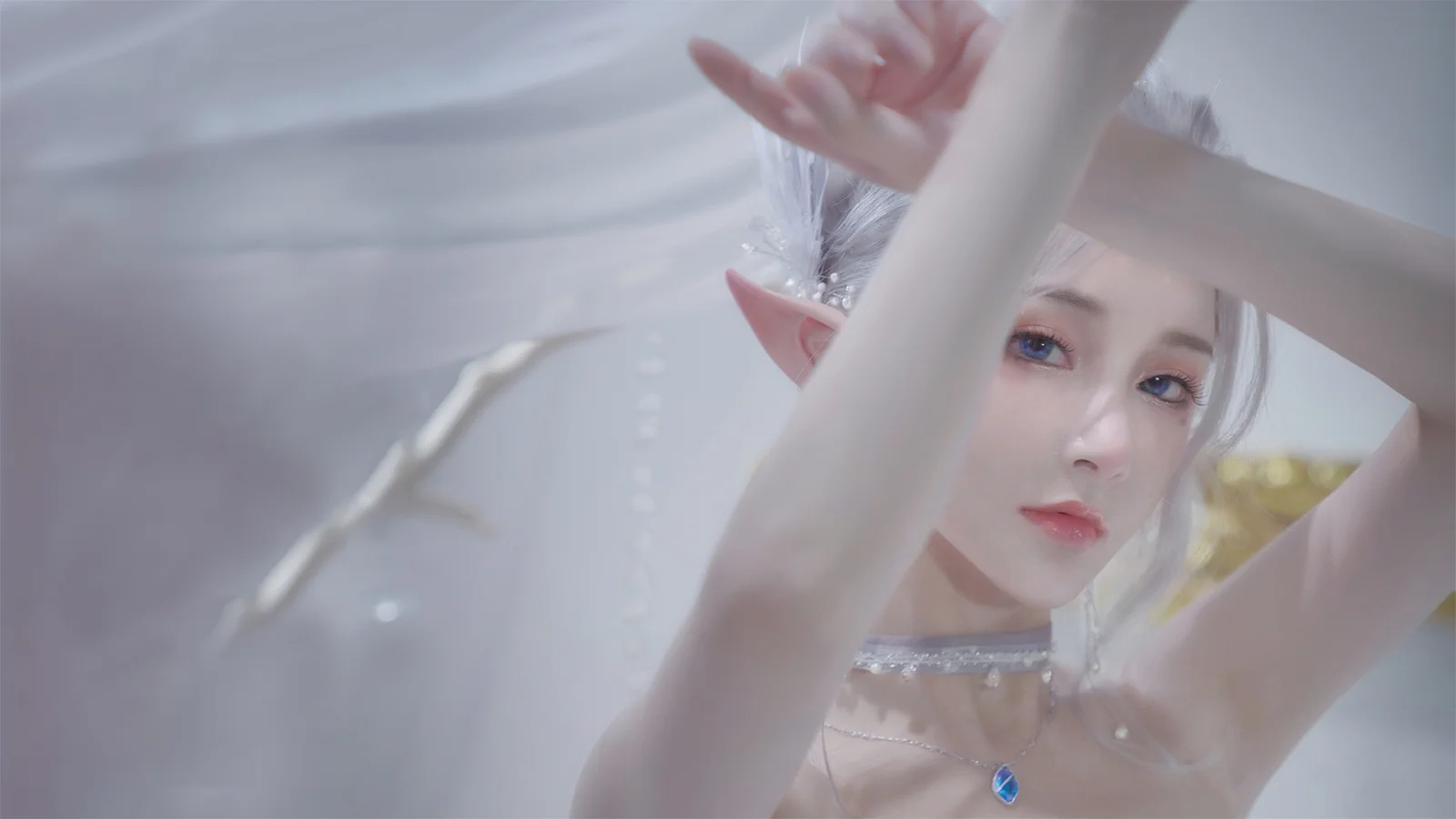 一位银发精灵造型的女性近距离面对镜头，柔和的浅色背景衬托出她的面容与尖耳朵。