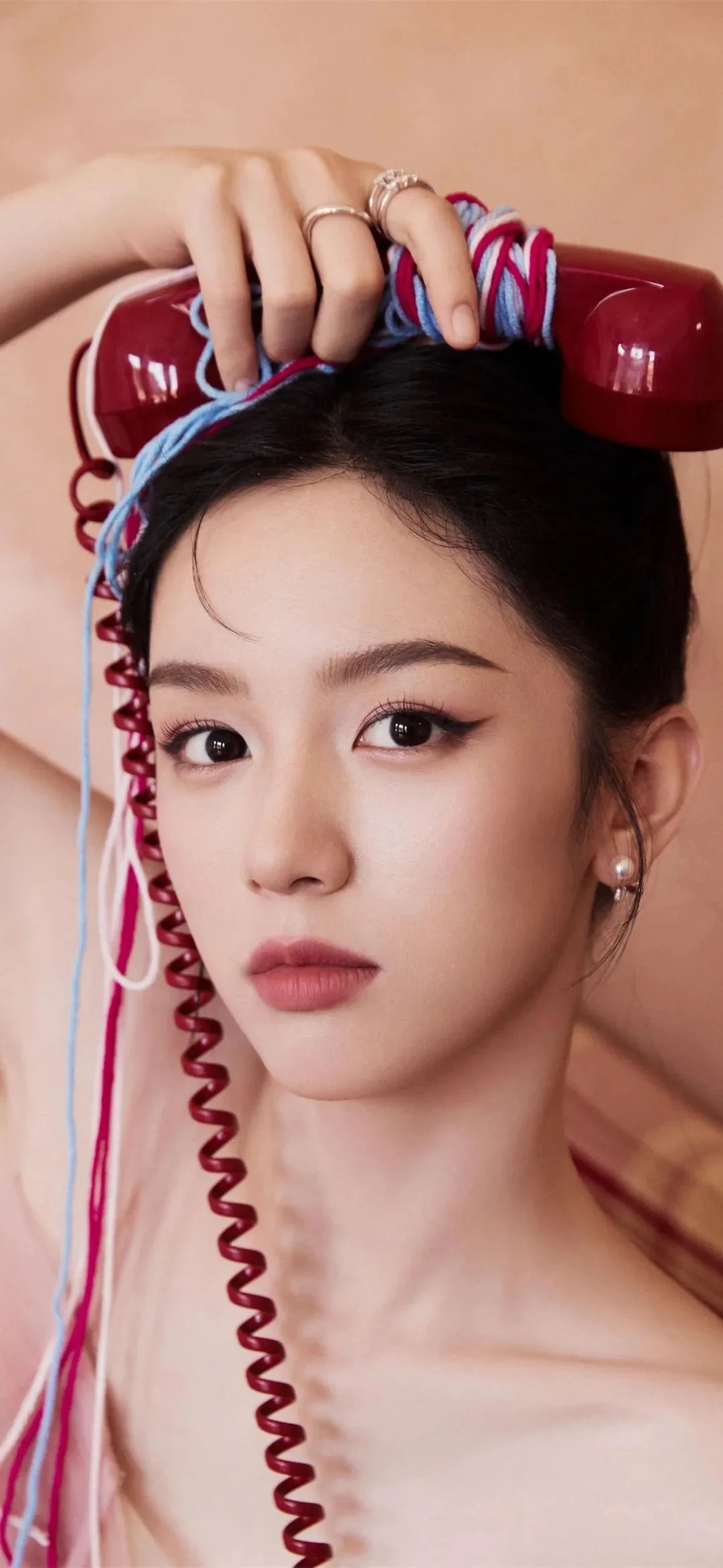 빨간 전화 수화기를 들고 머리에 알록달록한 헤어 롤러를 감은 여성의 클로즈업 초상이다.