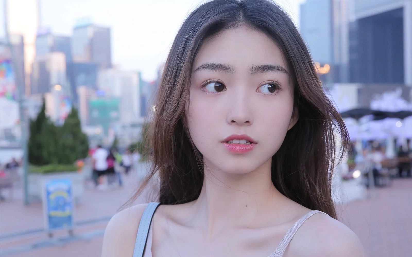 大人の女性が都会の通りでカメラに向かい、背景にはぼやけた建物と街並みが見えます。