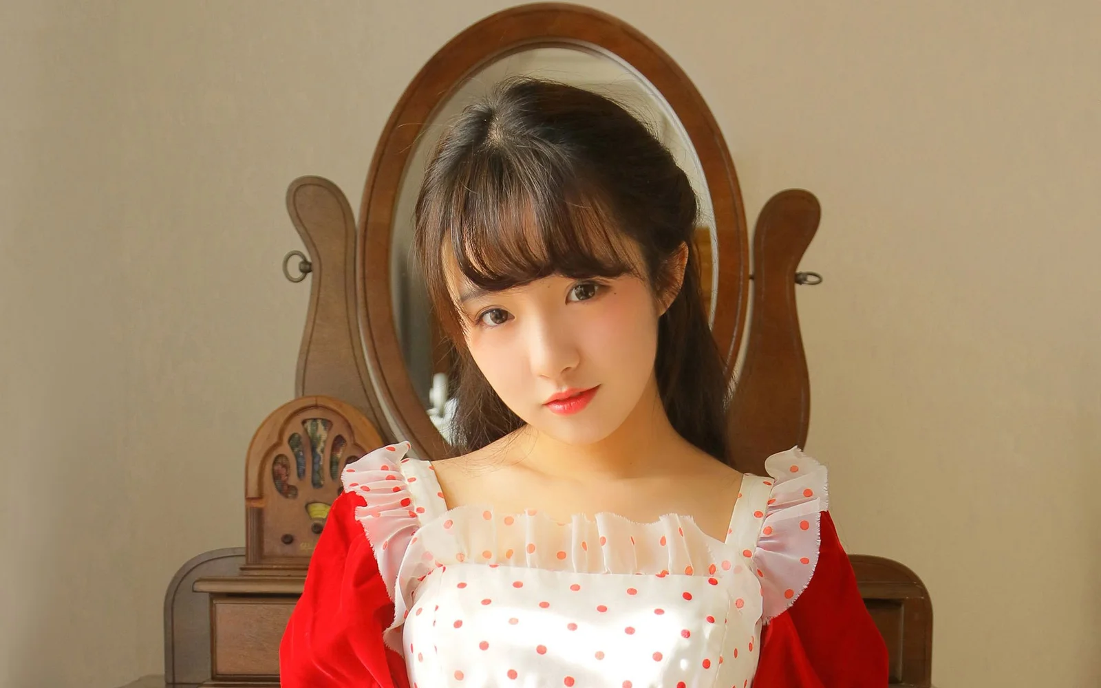 一名身穿红色上衣的女性坐在木质镜子前面对镜头。