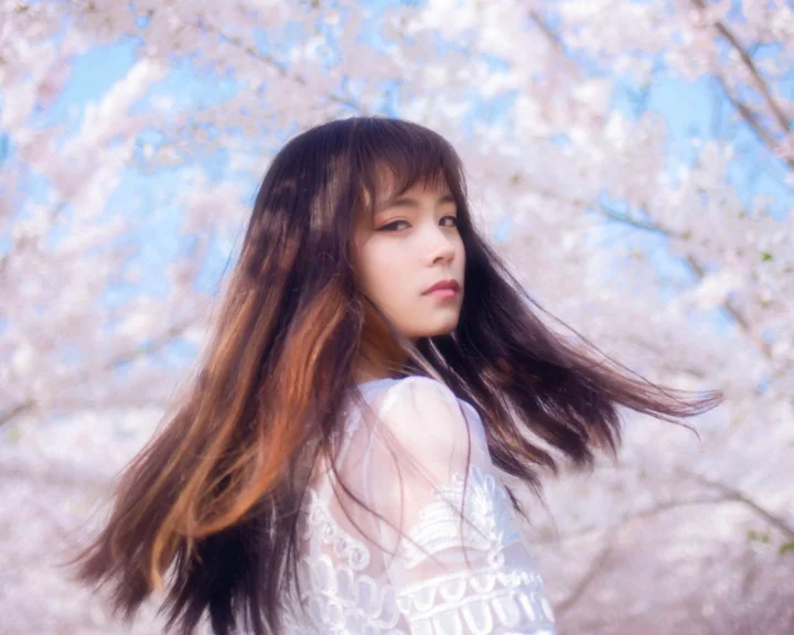 一名长发女子站在盛开的樱花树下回望镜头。