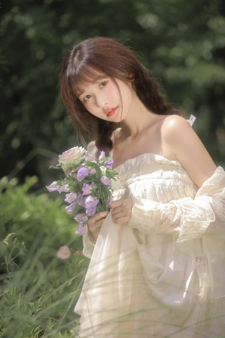一名女子在绿意盎然的花园中手捧紫色花束，身穿白色连衣裙。
