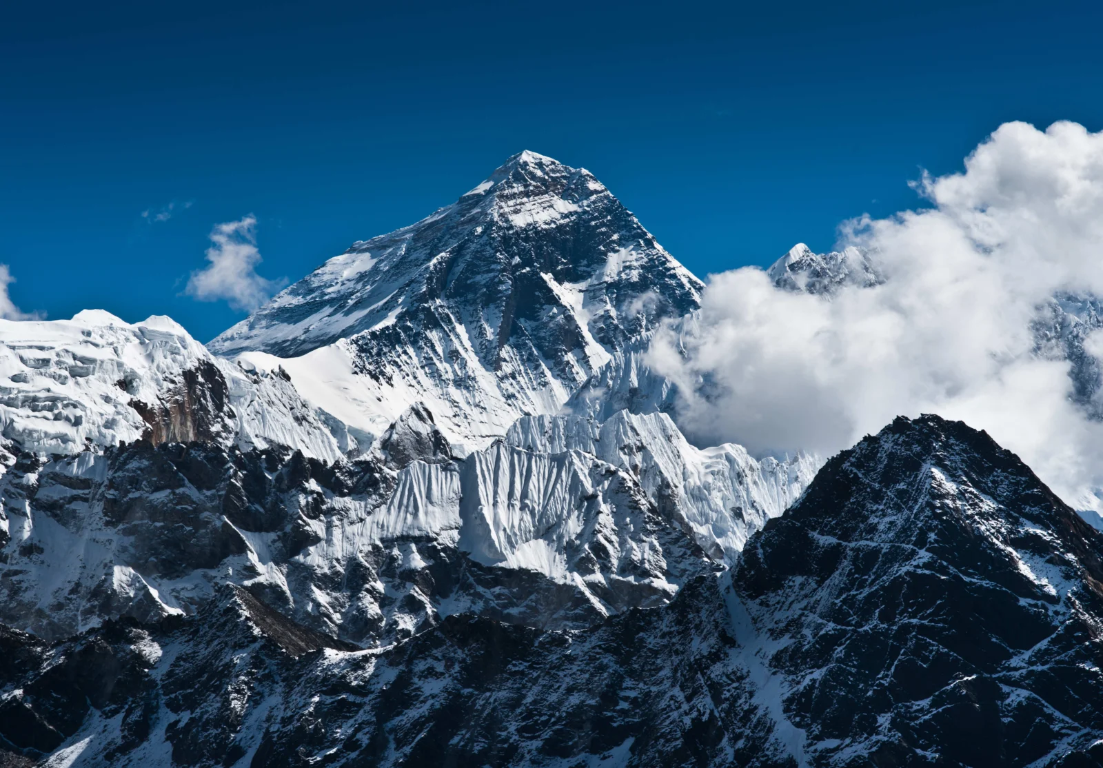 雄伟的雪山在蓝天下耸立，山腰和周围覆盖着冰雪与云雾。