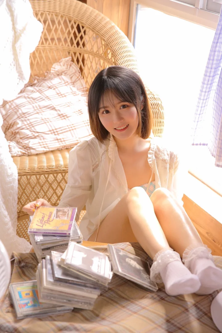 一名成年女性坐在明亮房间的藤编椅旁，周围散放着多张光盘。