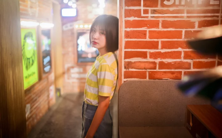 女性がレンガ壁と室内の座席のそばに立っています。