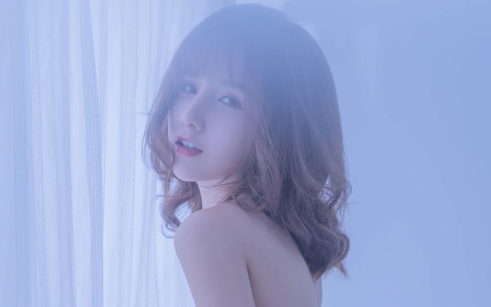 一位成年女性在窗帘旁以柔和蓝色光线呈现侧身人像。