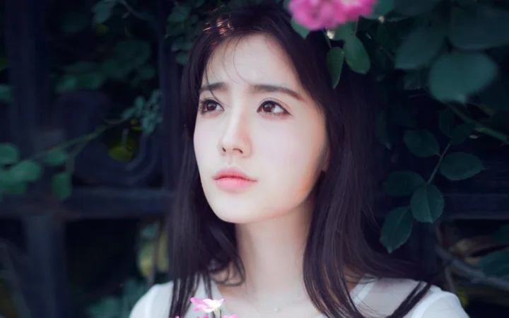 一名女性在深色绿叶和粉色花朵环绕下的近距离肖像。