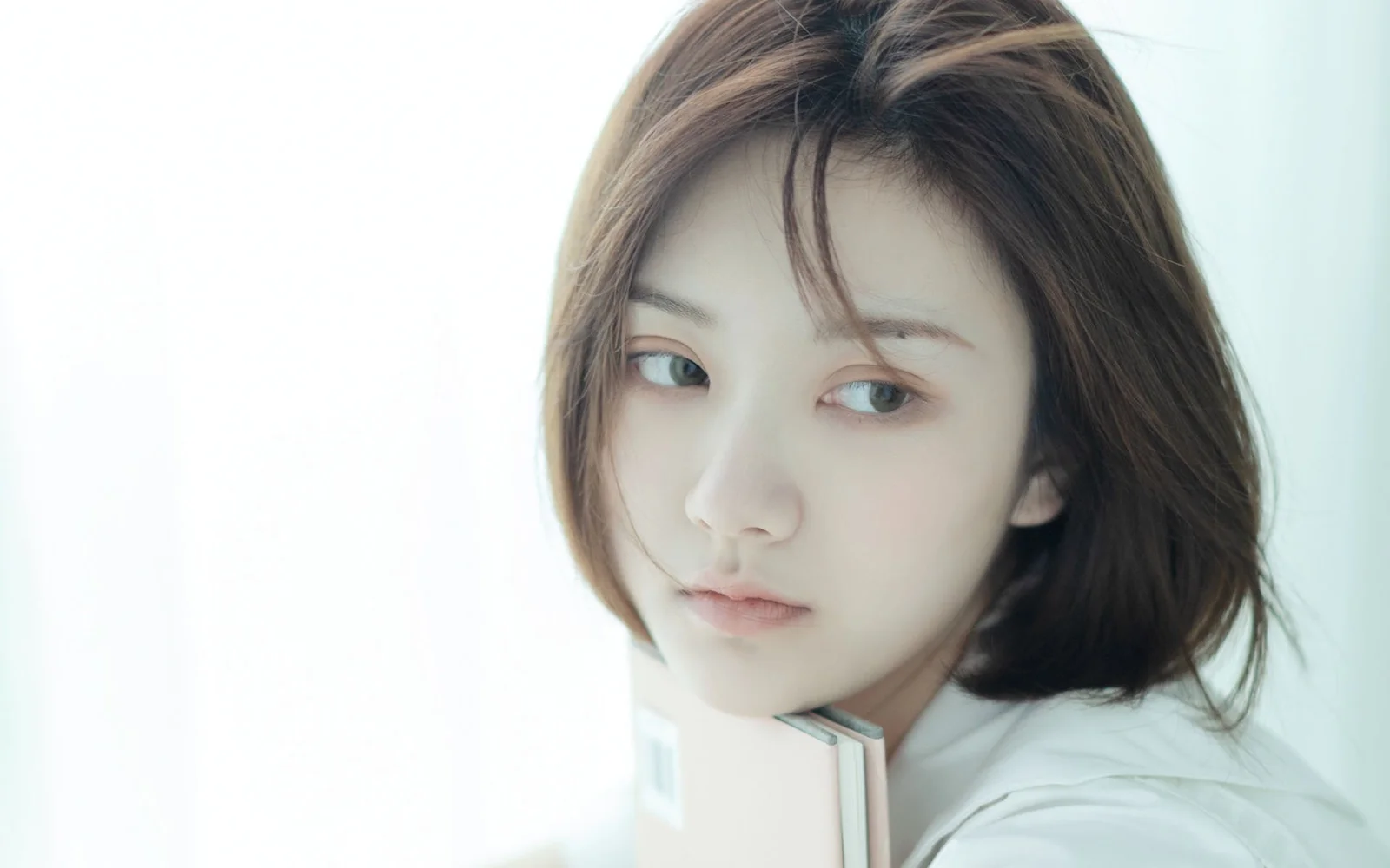 明るい背景の前で、茶色の短い髪の成人女性が淡い色の本を持つクローズアップポートレート。