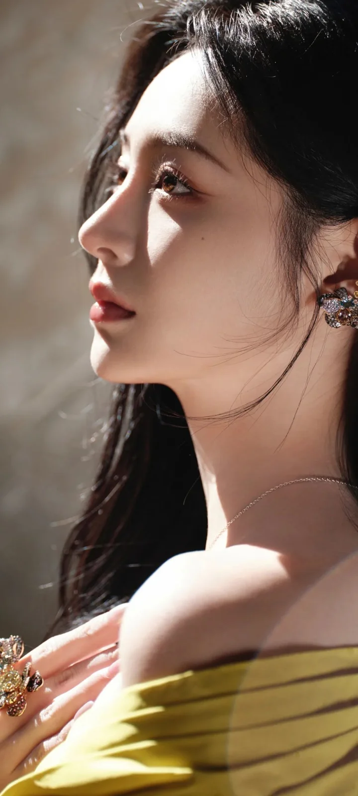 一名佩戴耳飾、身穿黃色露肩服裝的成年女性側臉肖像沐浴在柔和光線中。