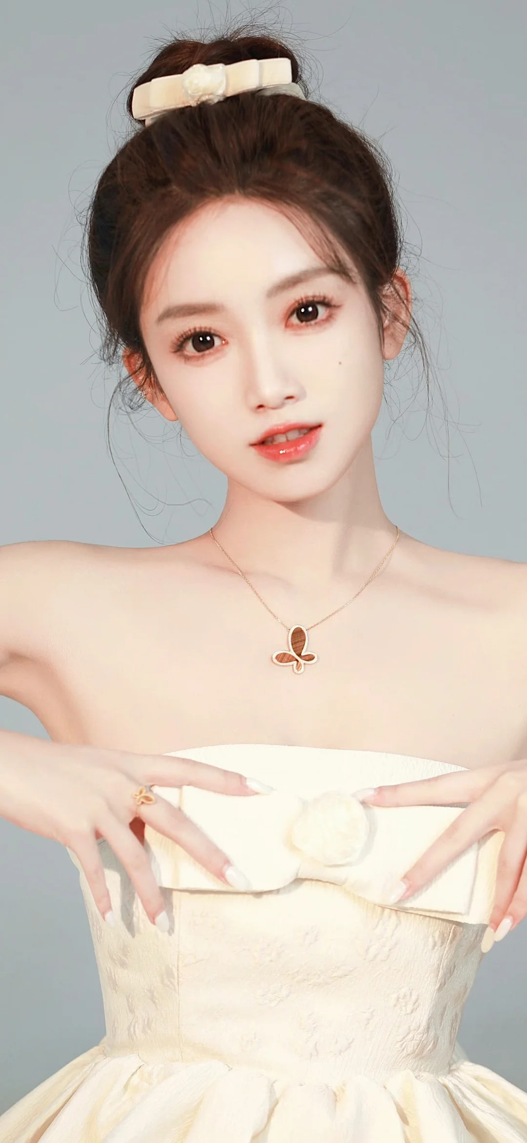머리를 올려 묶은 여성이 흰색 튜브톱 드레스를 입고 밝은 회색 배경 앞에서 카메라를 바라보고 있습니다.