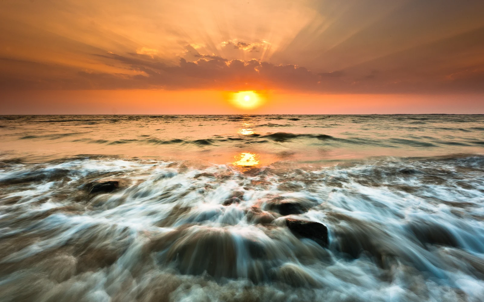 夕阳映照着海面，海浪在岸边翻涌并反射出金色光芒。