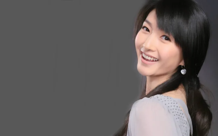 一位黑发女子面带微笑，转身看向镜头，身后是纯灰色背景。