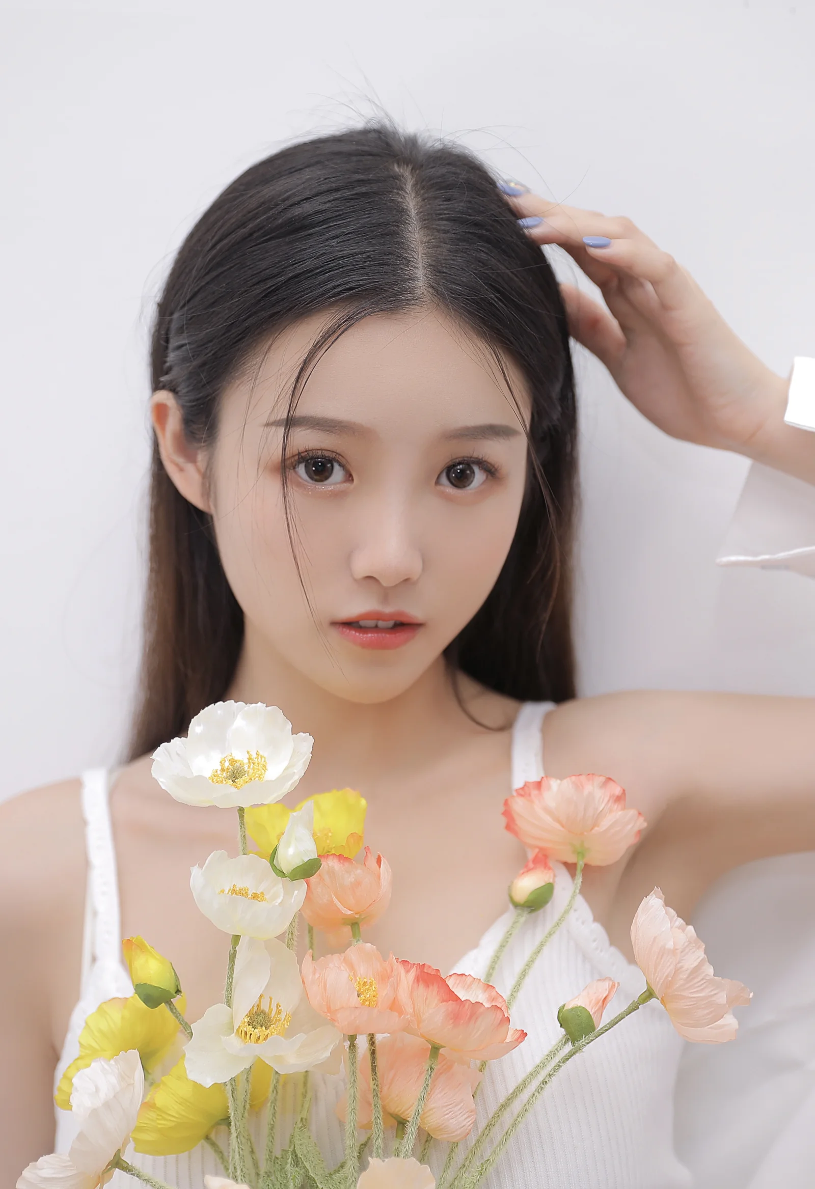 一位女性手持鲜花站在浅色背景前的竖幅人像照片。