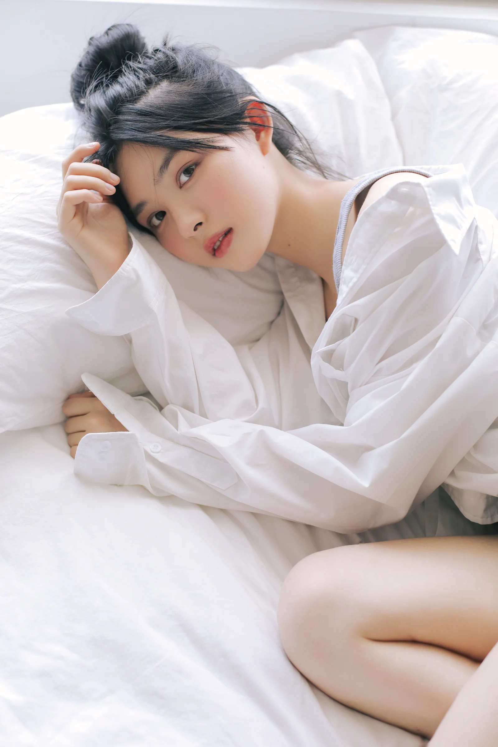 一名成年女子穿着宽松白衬衫侧卧在白色床铺上。