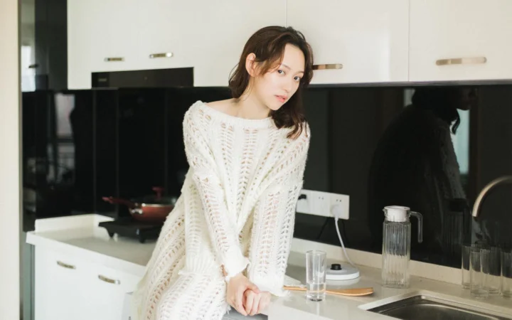 一名成年女子穿着白色针织衫站在现代厨房中。