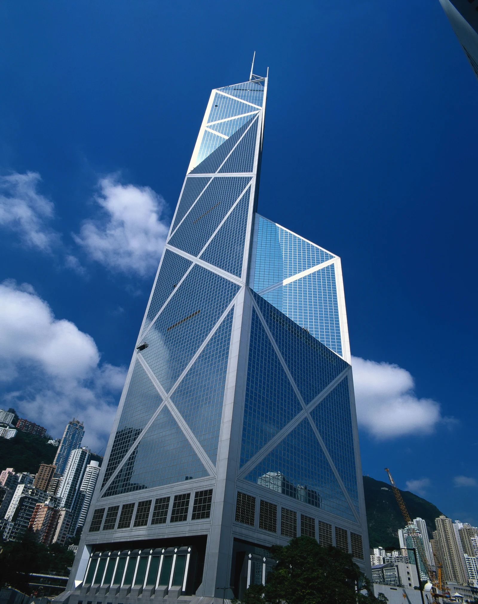 仰拍视角下，一座高耸的玻璃幕墙建筑矗立在蓝天白云与城市高楼之间。