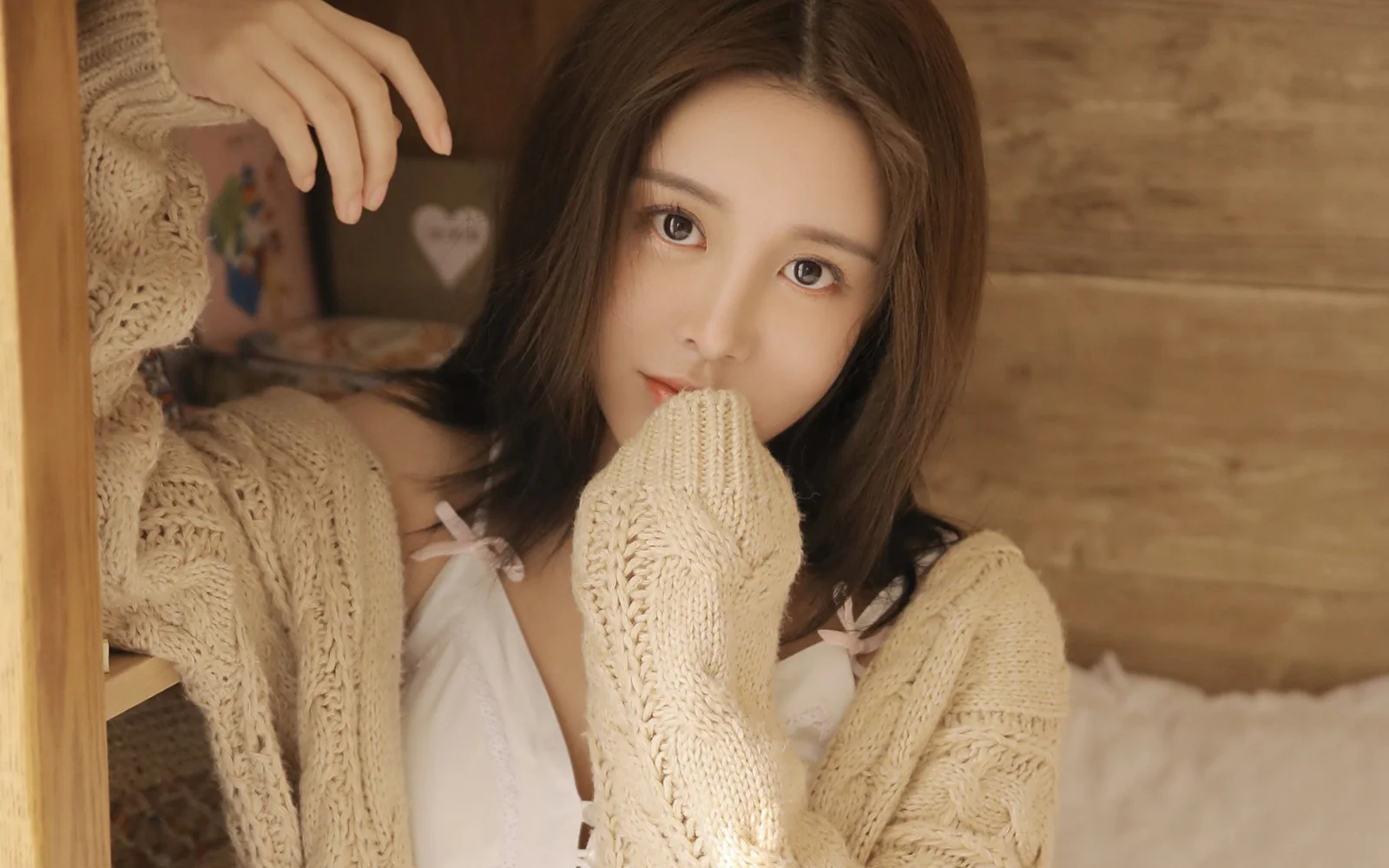 一名成年女性穿著米色針織開襟衫，在溫暖的木質室內環境中面向鏡頭。