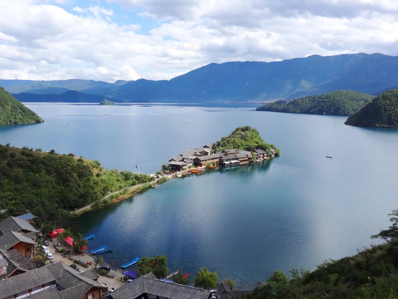 青い湖を山々と森林、湖畔の集落が囲み、白い雲が浮かぶ空が広がっています。
